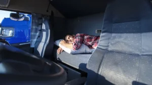 A picture of a truck driver taking a rest in the bunk in his truck cab